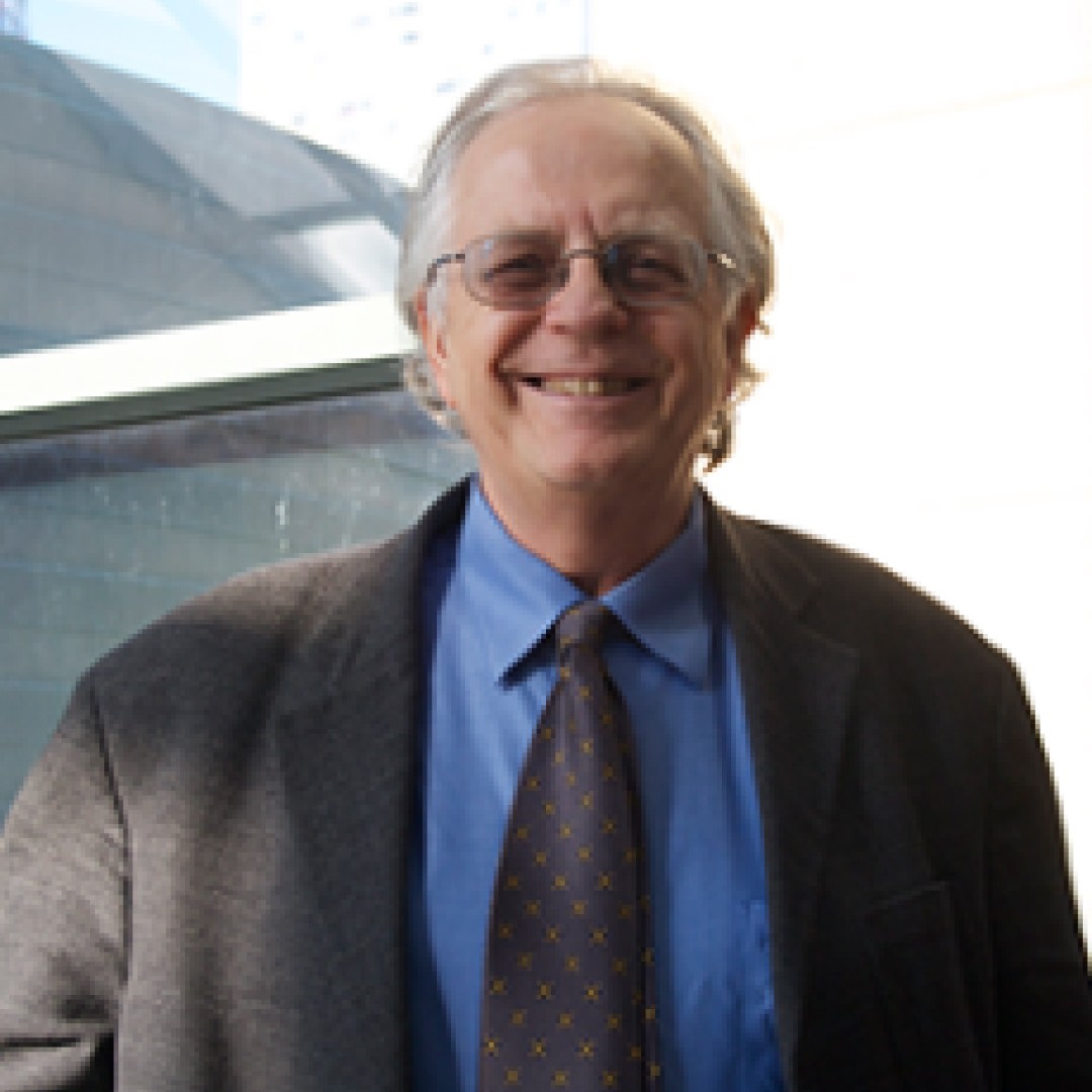 Close-up headshot of Charles Davis smiling. He has grey hair and glasses, and is wearing a grey suit jacket with a blue shirt and patterned tie.