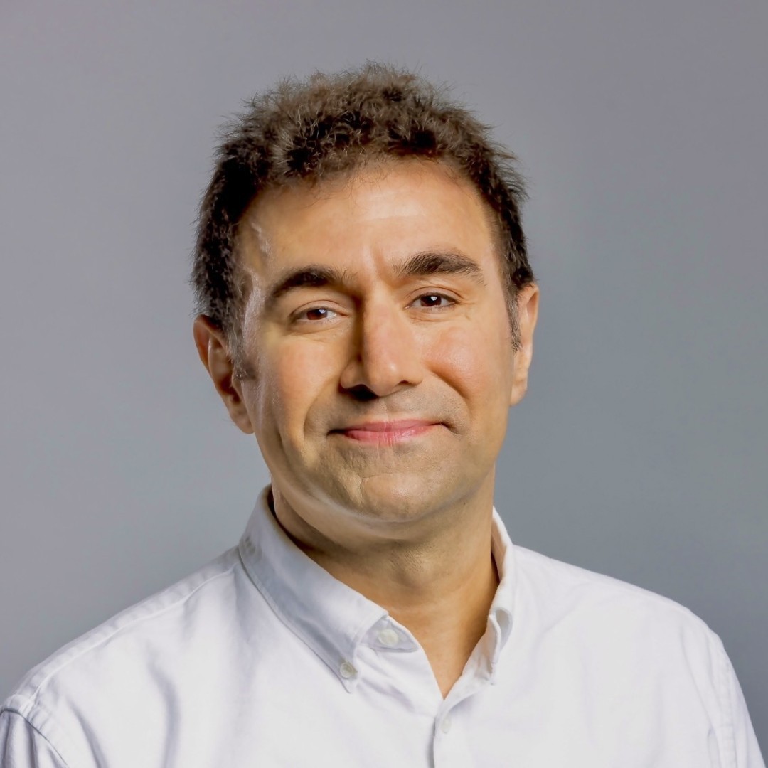 Close-up headshot of Hossein Rahnama smiling. He has short curly hair and is wearing a white button-up shirt.