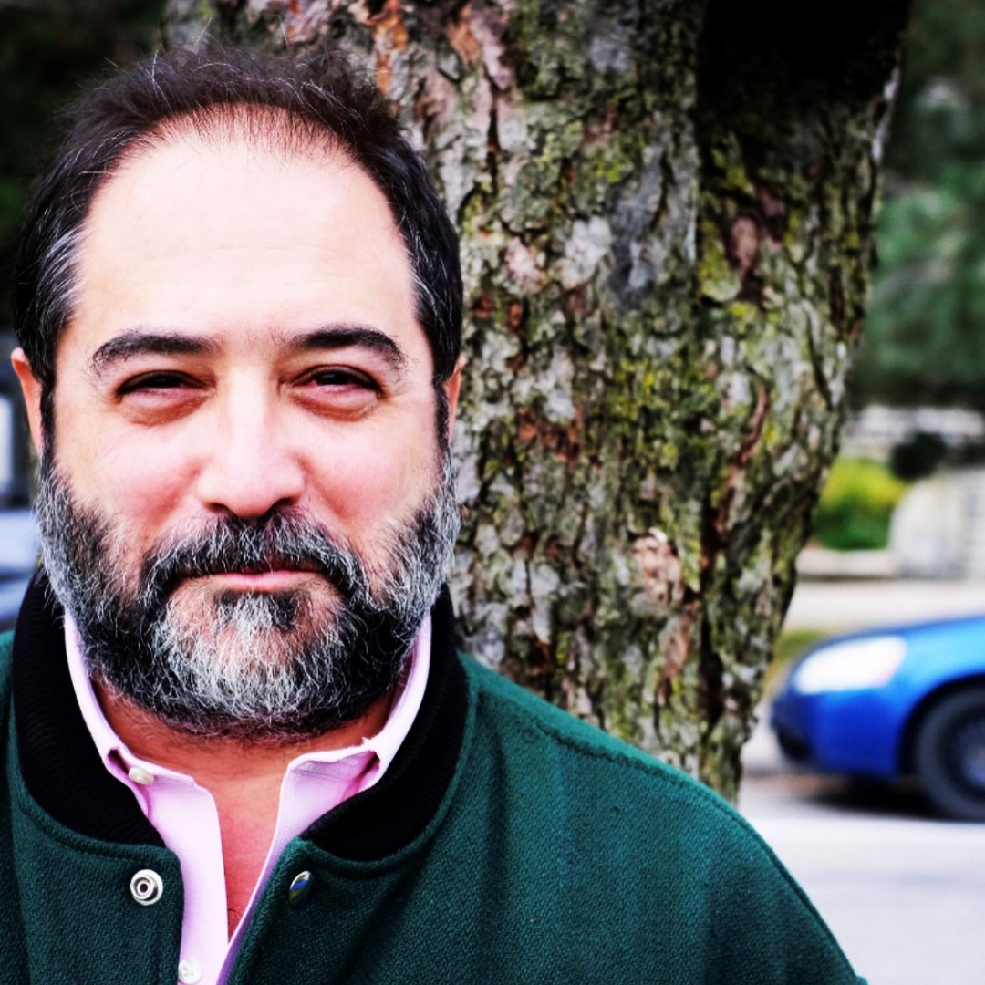 Close-up headshot of James Nadler smiling. He has short hair and is wearing a dark suit jacket, striped shirt, and dark tie.