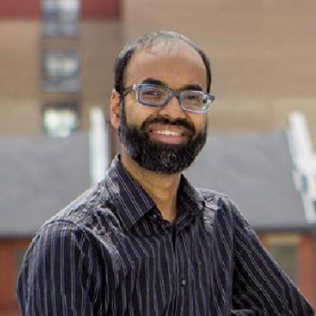Close-up headshot of Richard W. Lachman smiling. He has a beard, glasses, and is wearing a black and grey striped shirt.