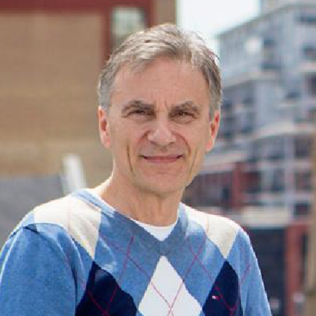 Close-up headshot of Steven Ehrlick smiling. He has short grey hair and is wearing a blue argyle sweater over a white shirt.